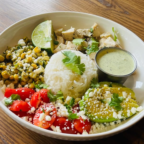 A vibrant Montage Wine Bar & Spirits chicken bowl with rice, corn, tomatoes, avocado, and lime.