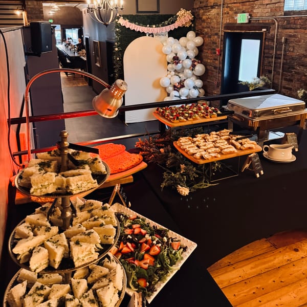 A buffet table with various appetizers, including sandwiches, bruschetta, and salad, under a heat lamp.