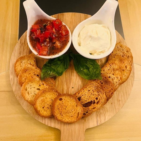 Bruschetta with tomato and cheese dips, basil leaves, and toasted bread on a wooden board.