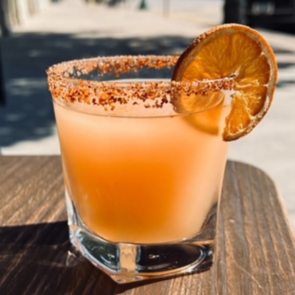 A Montage Wine Bar cocktail with a spiced rim and dried orange slice on a wooden table.