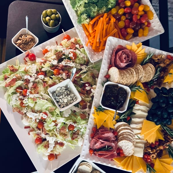 A buffet spread with Caesar salad, a vegetable platter, and a charcuterie board.
