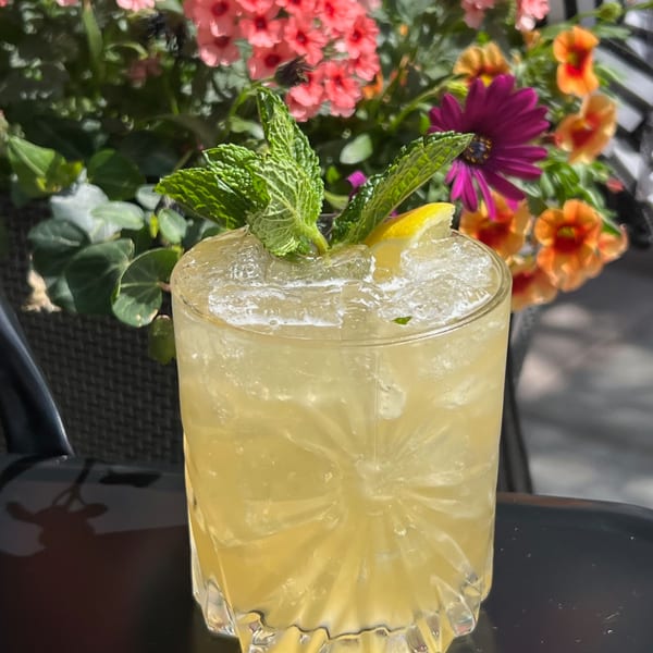 A refreshing cocktail with mint and lemon garnish, set against a vibrant floral background.