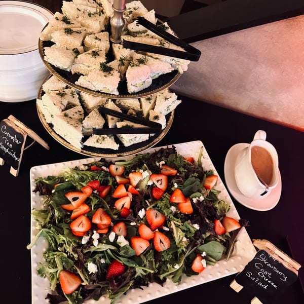 A tiered tray of cucumber tea sandwiches and a strawberry goat cheese salad on a black table.