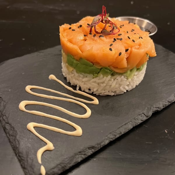 Salmon tartare with avocado and rice, garnished with black sesame seeds and microgreens, on a slate plate.